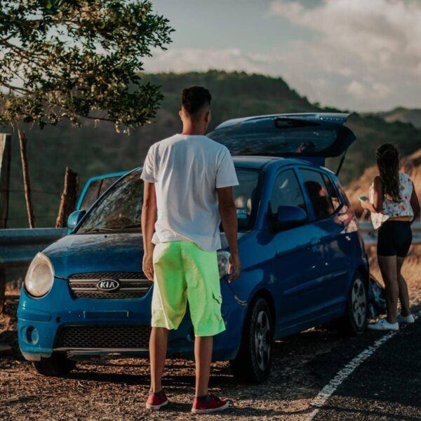 Two people driving in a modern Kia, city skyline outside, smiling and relaxed