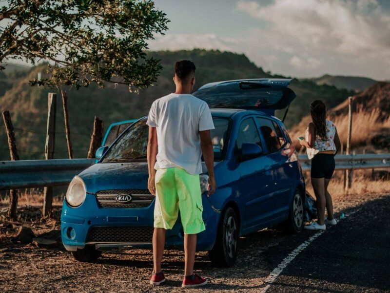 Two people driving in a modern Kia, city skyline outside, smiling and relaxed